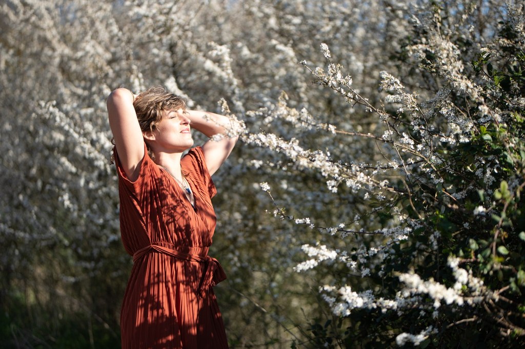 Camille Soustra en robe terracotta, souriante au milieu des fleurs blanches